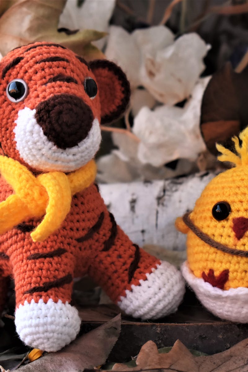 Crochet stuffed tiger and chick among autumn leaves, perfect for seasonal decor.