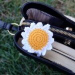 Detailed view of a crochet sunflower accessory on an open handbag outdoors.