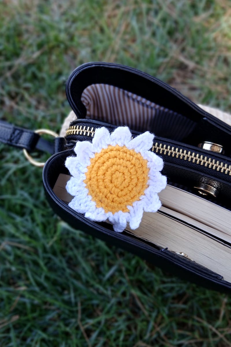 Detailed view of a crochet sunflower accessory on an open handbag outdoors.