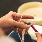 A focused shot of hands crocheting with a pink hook and white yarn, showcasing the art of crafting.
